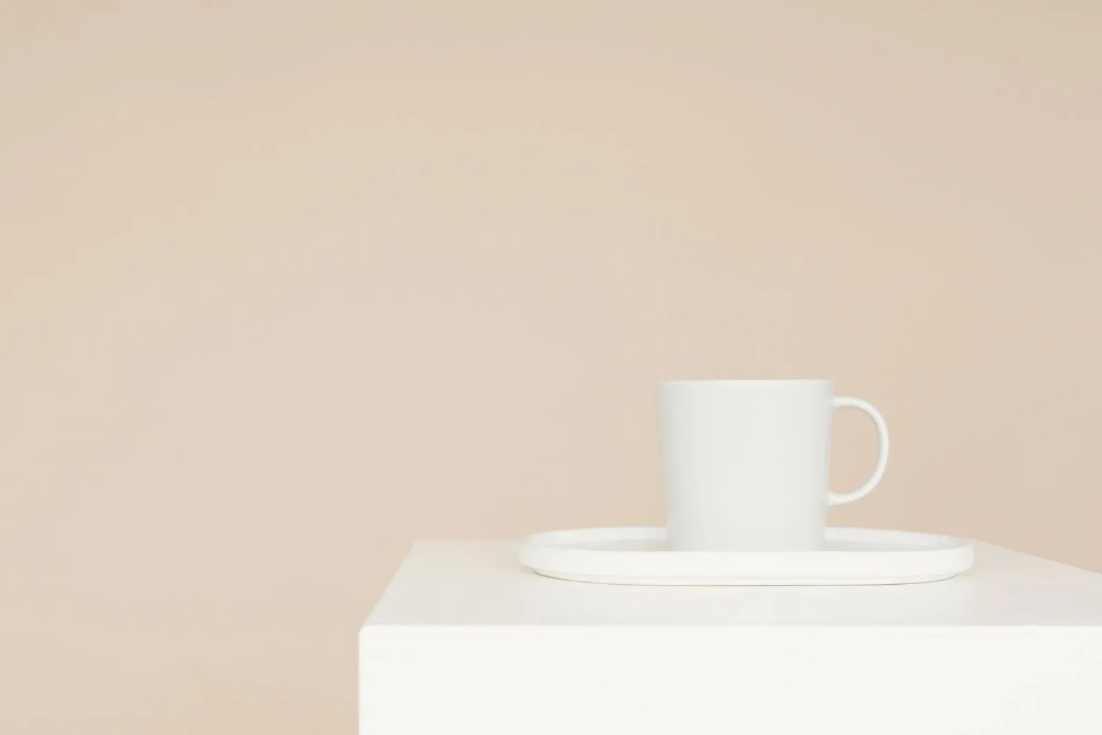 A white ceramic mug on a tray atop a white plinth